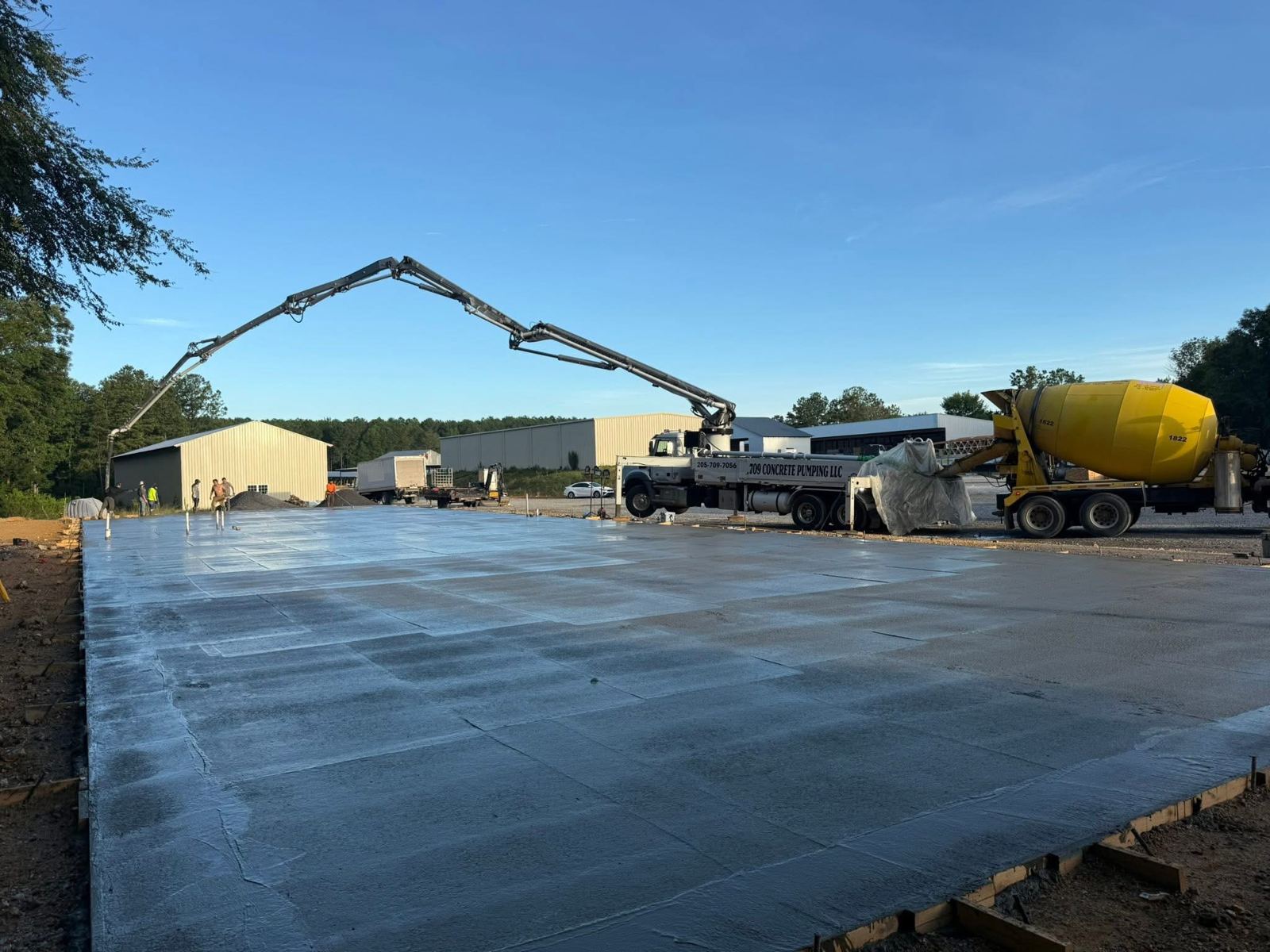 A concrete pump truck pouring a large slab beside metal buildings